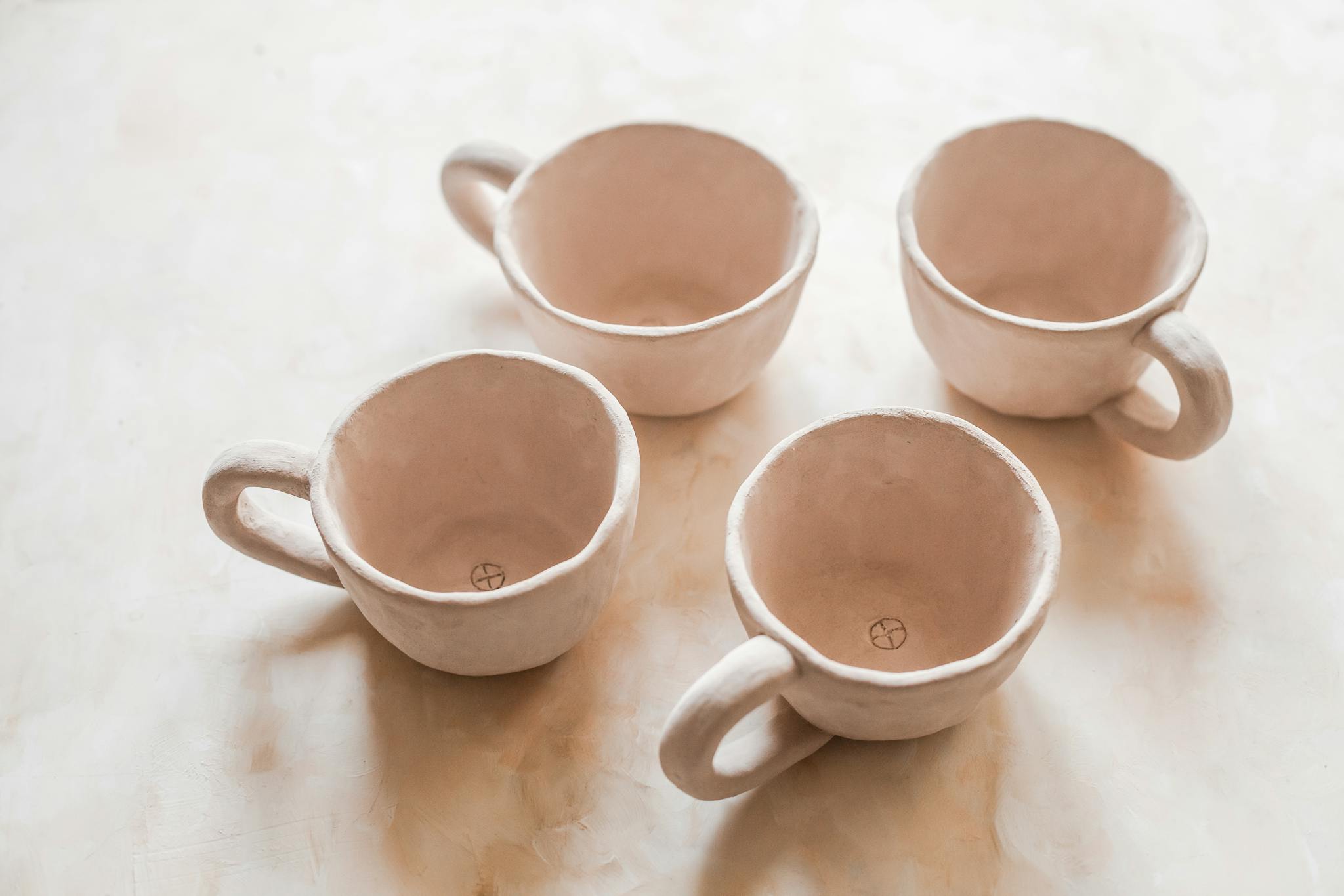 Four handcrafted beige ceramic cups on a light background showcasing a minimalist design.